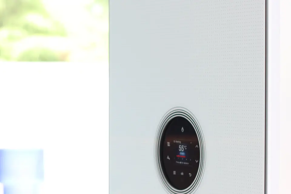 Wall-mounted gas boiler with a round digital control display beside a kitchen window