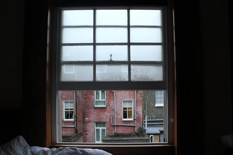 Condensation fogging the upper panes of a sash window in a bedroom, with a red brick building outside