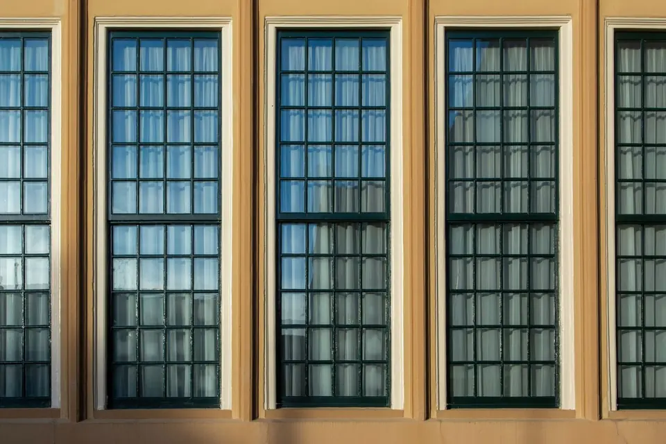 Close view of tall timber sash windows with small glazing bars and painted frames in a rendered wall