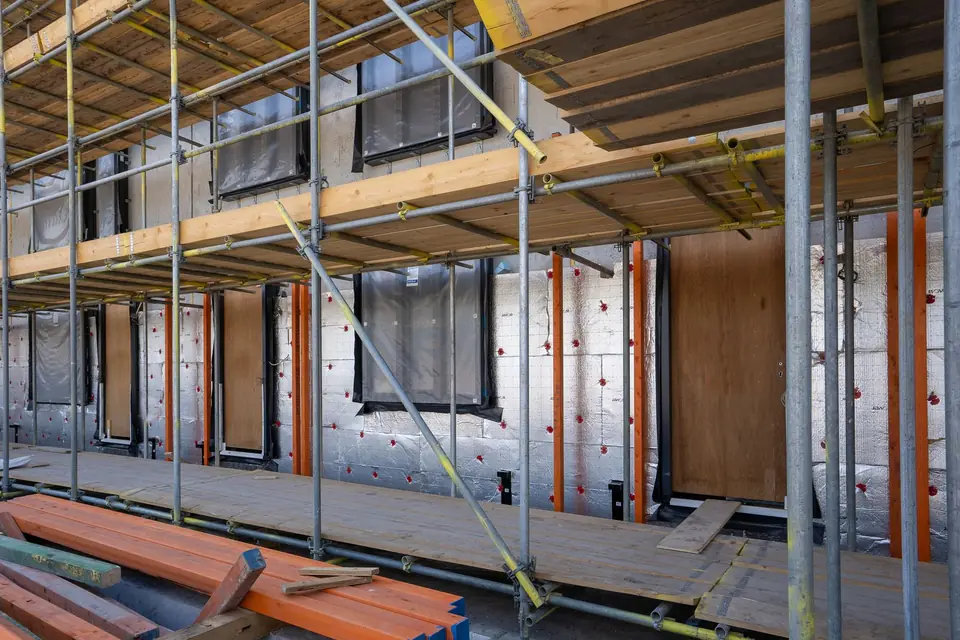 Foil-faced insulation boards fixed to a house wall with red plastic fixings, seen behind scaffolding