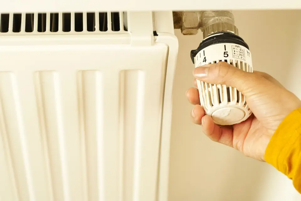 Hand in a yellow sleeve turning the thermostatic valve on a white panel radiator