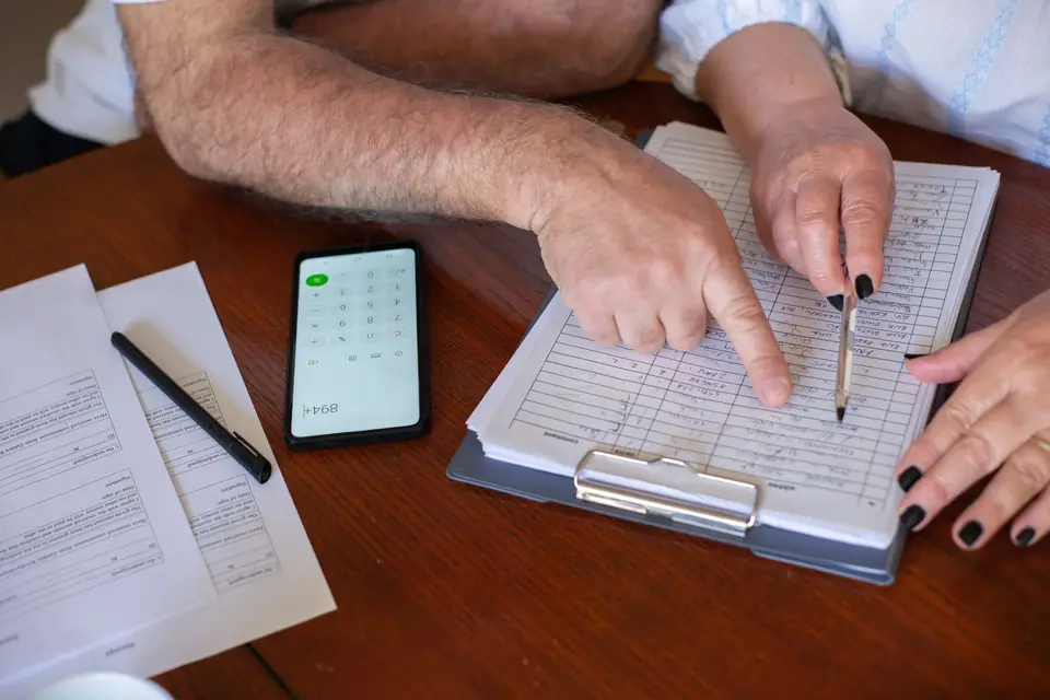 Hands going through billing paperwork on a table, with a pen, a phone calculator and a page of figures