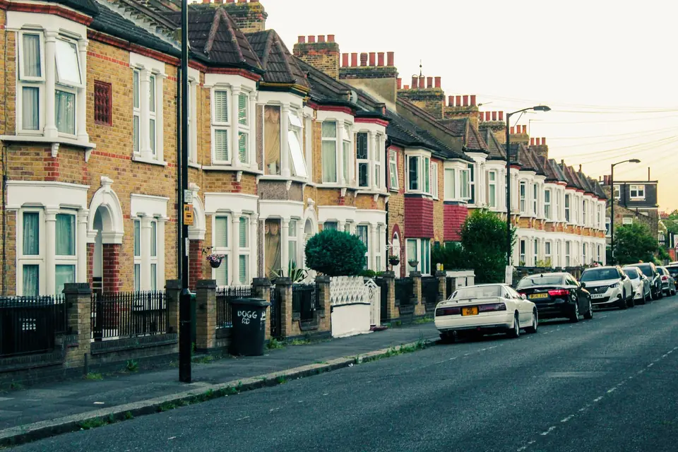 Row of brick Victorian terraced houses with bay windows and parked cars on a London street