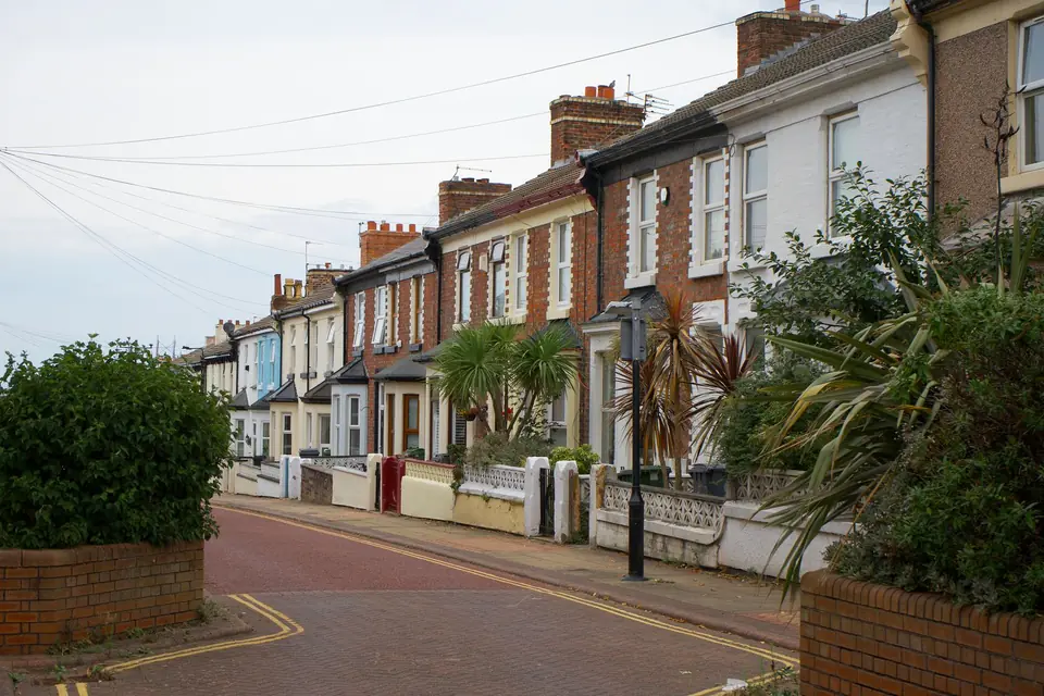 Row of two-storey brick terraced houses with small walled front gardens and bay windows on a quiet block-paved street