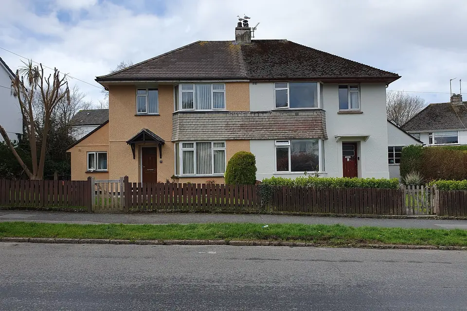 Rendered semi-detached pair with a hipped tiled roof, front bay windows and a low wooden picket fence