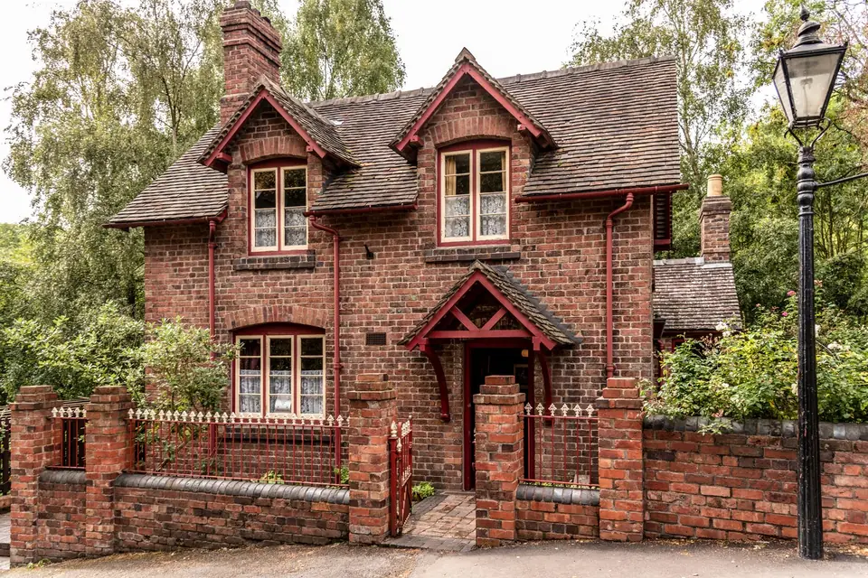 Two storey red brick detached house with gabled roof, bay windows, front garden and iron railings