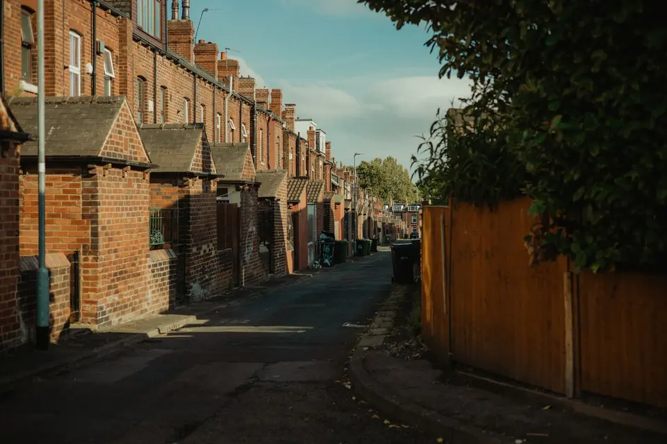 Red brick terraced houses with porches and chimney stacks along a narrow street in Leeds in evening sun