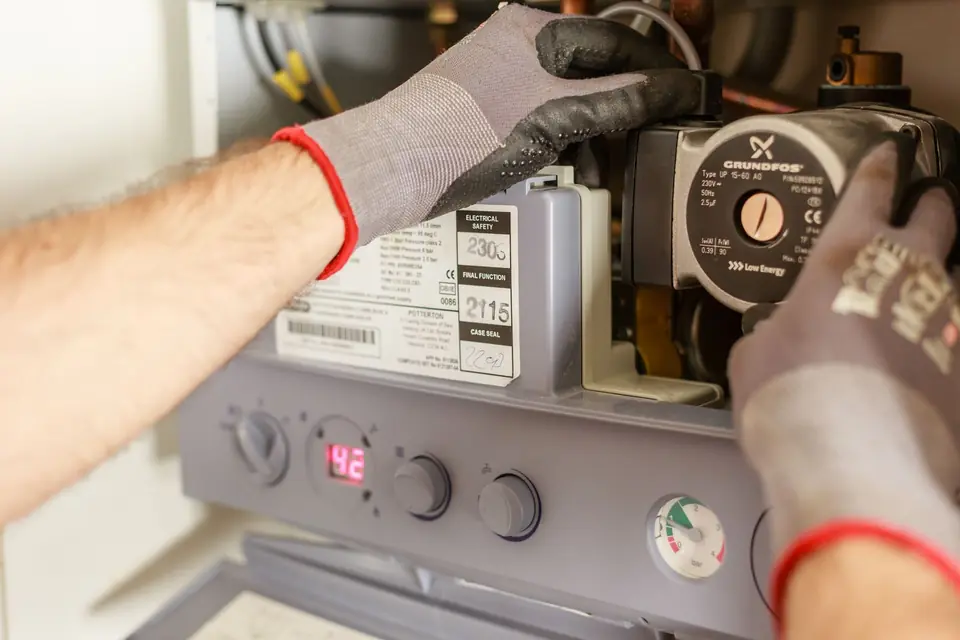 Gloved hands of a heating engineer adjusting the pump inside an open wall-mounted gas combi boiler