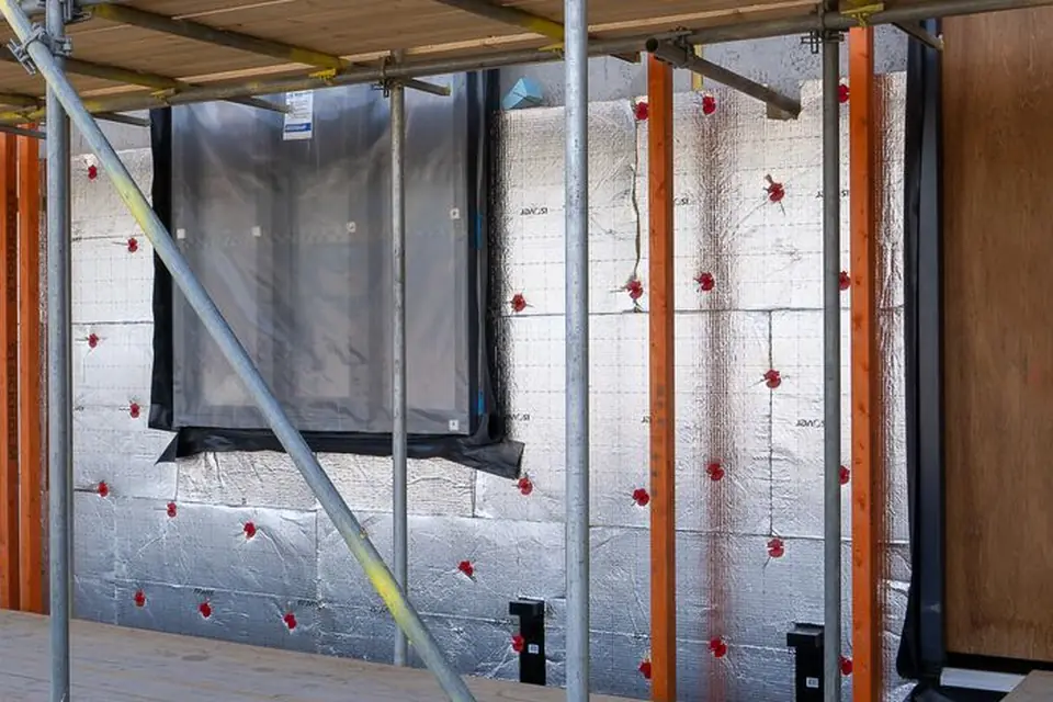 Foil-faced insulation boards fixed to the wall of a house with red fixing caps, seen behind scaffolding