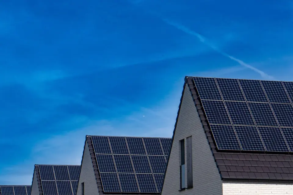 Row of modern gabled houses with black solar panel arrays on their tiled roofs under a clear blue sky