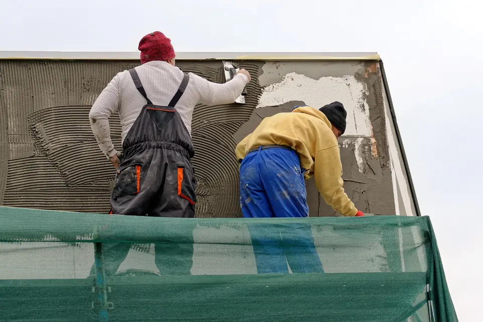 Two renderers on scaffolding trowel base coat render over white insulation boards on a house wall