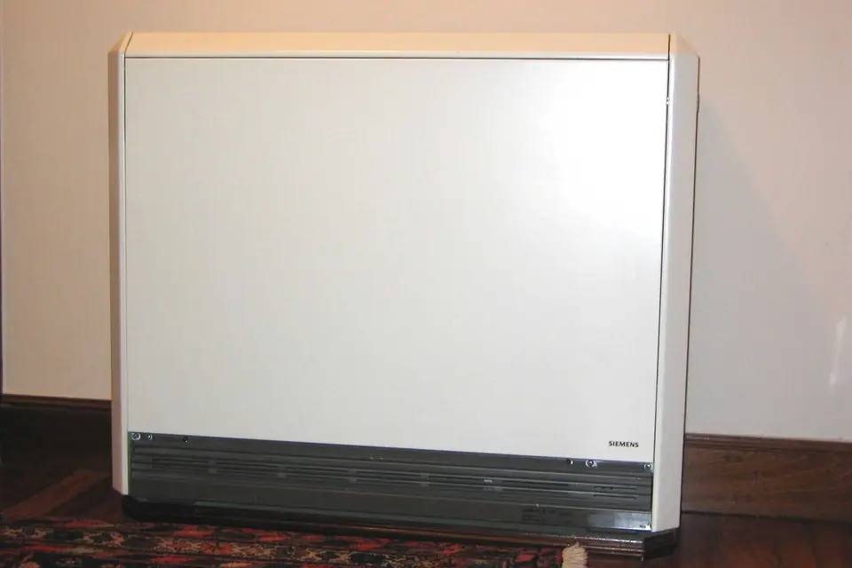 White electric night storage heater standing against a wall on a wooden floor in a home