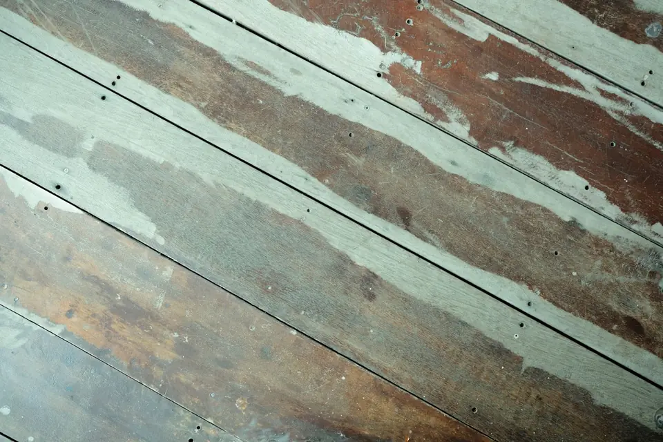 Close-up of worn bare timber floorboards with visible nail heads and patches of flaking old paint