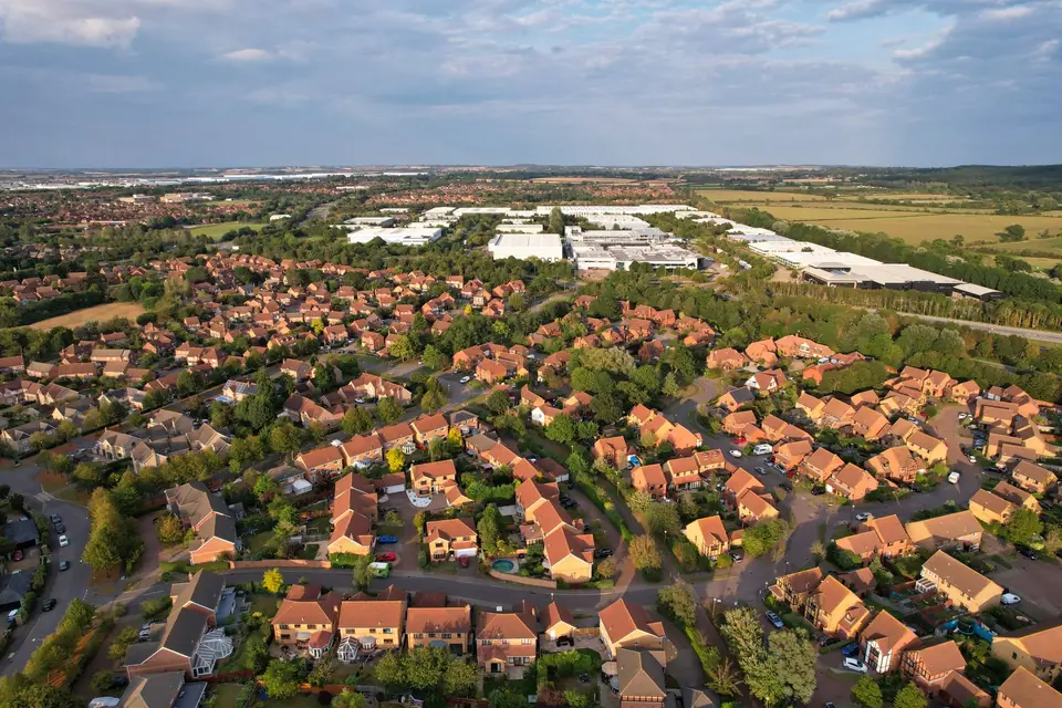 Aerial view of a modern housing estate with red brick houses and tiled roofs, fields and warehouses beyond